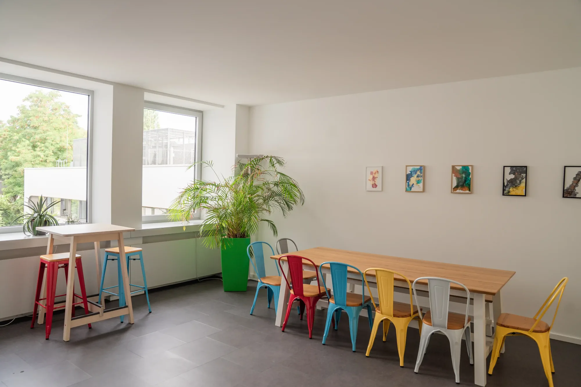 Aufenthaltsbereich mit langem Holztisch, bunten Stühlen und Kunstwerken im Schlump One, Hamburg